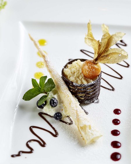 Salzburgerland: wellness hotel with 4 stars and cuisine Artfully plated dessert with chocolate, physalis, and berries on a white plate