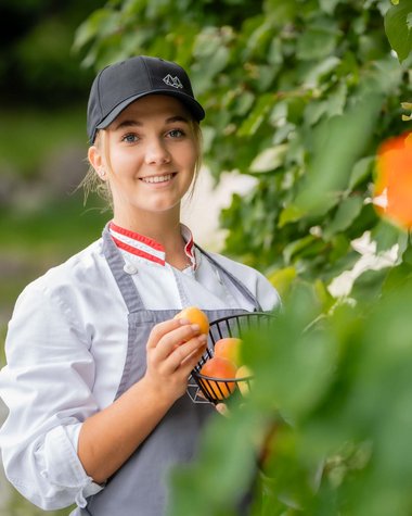 Wildkogel: Hotel mit Blick für das Besondere Junge Frau in Kochkleidung pflückt Aprikosen von einem Baum