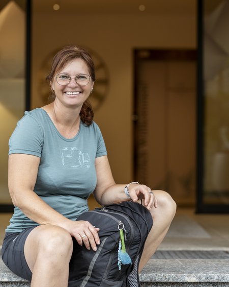 Familienhotel im Salzburger Land: Smaragdhotel Tauernblick Frau mit Brille und Rucksack sitzt lächelnd vor einem Gebäude