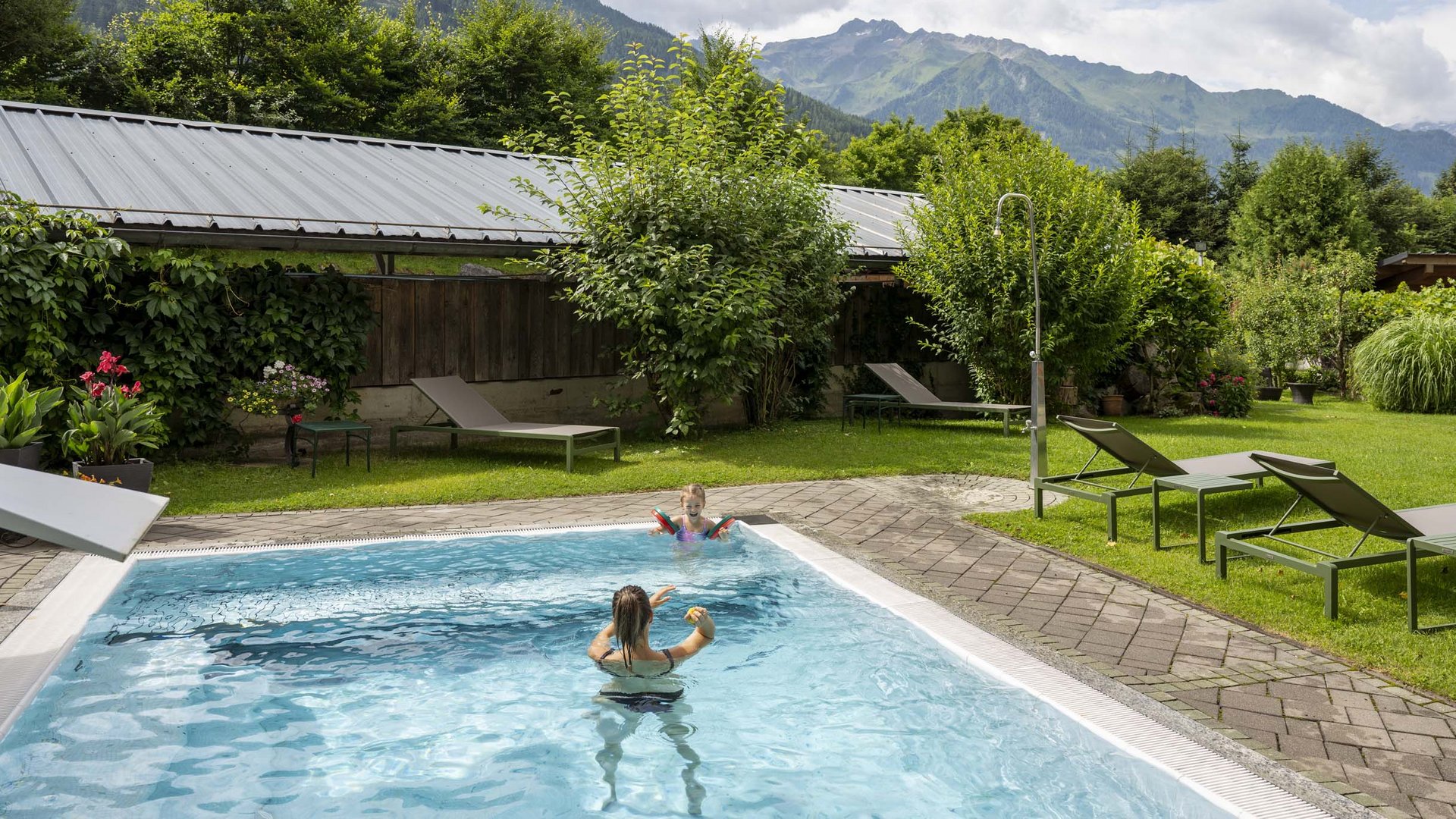 Family hotel in Austria with pool Swimming pool in garden with mountains in background and children playing in water