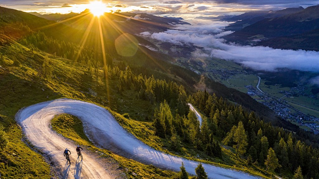 Nationalpark Hohe Tauern: Urlaub für Biker Zwei Radfahrer auf Bergstraße bei Sonnenuntergang mit Tal und Wolken darunter