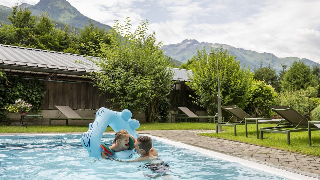 Wellnesshotel Salzburgerland: Smaragdhotel Tauernblick Mann spielt mit Kind im Pool mit Bergblick und Liegestühlen im Garten