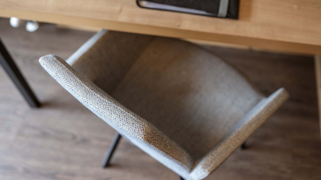 Smaragdhotel Tauernblick – Ihr 4-Sterne-Hotel am Wildkogel Blick von oben auf einen grauen Bürostuhl neben einem Holztisch mit Notizbuch