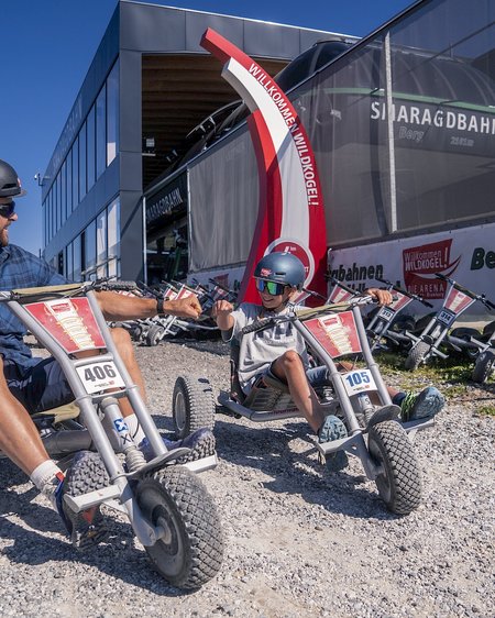 Hotel in Bramberg: Smaragdhotel Tauernblick Vater und Sohn geben sich einen Faustgruß auf Mountaincarts in Wildkogel