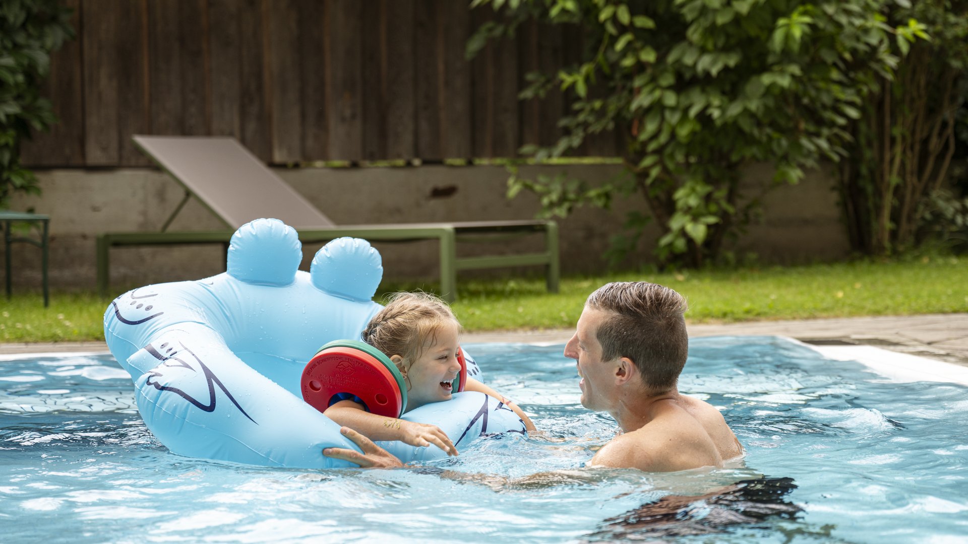 Wasserspaß im Hotel in Österreich mit Pool Mann spielt mit lachendem Kind im Schwimmbad mit blauem Schwimmflügel