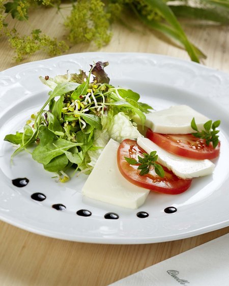 Salzburgerland: wellness hotel with 4 stars and cuisine Tomato mozzarella salad on white plate with greens and balsamic dots