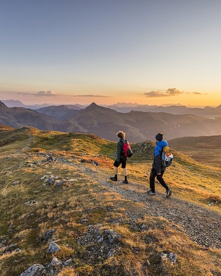 Einmaliges Wanderhotel im Salzburgerland Zwei Wanderer auf Bergweg bei Sonnenuntergang mit Aussicht auf Berge
