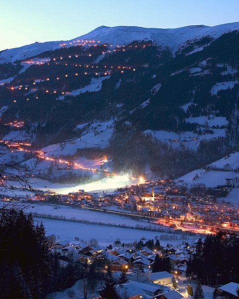 Salzburgerland: Winter im Smaragdhotel Tauernblick Winterdorf mit beleuchtetem Skigebiet am Berghang in der Abenddämmerung