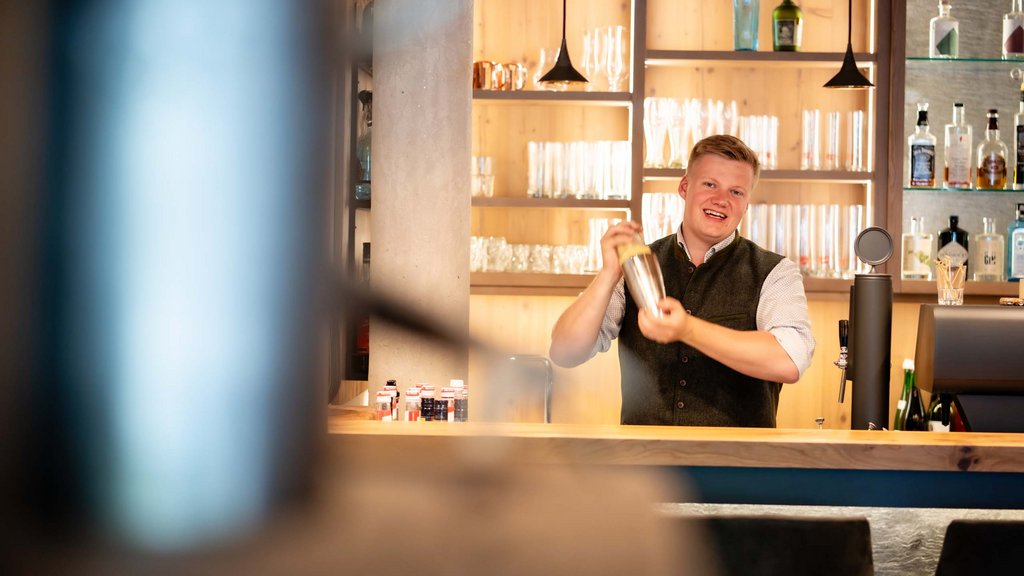 Ihr Pärchenurlaub in Österreich Barkeeper schüttelt Cocktailshaker in moderner Bar mit Holzregalen und Flaschen