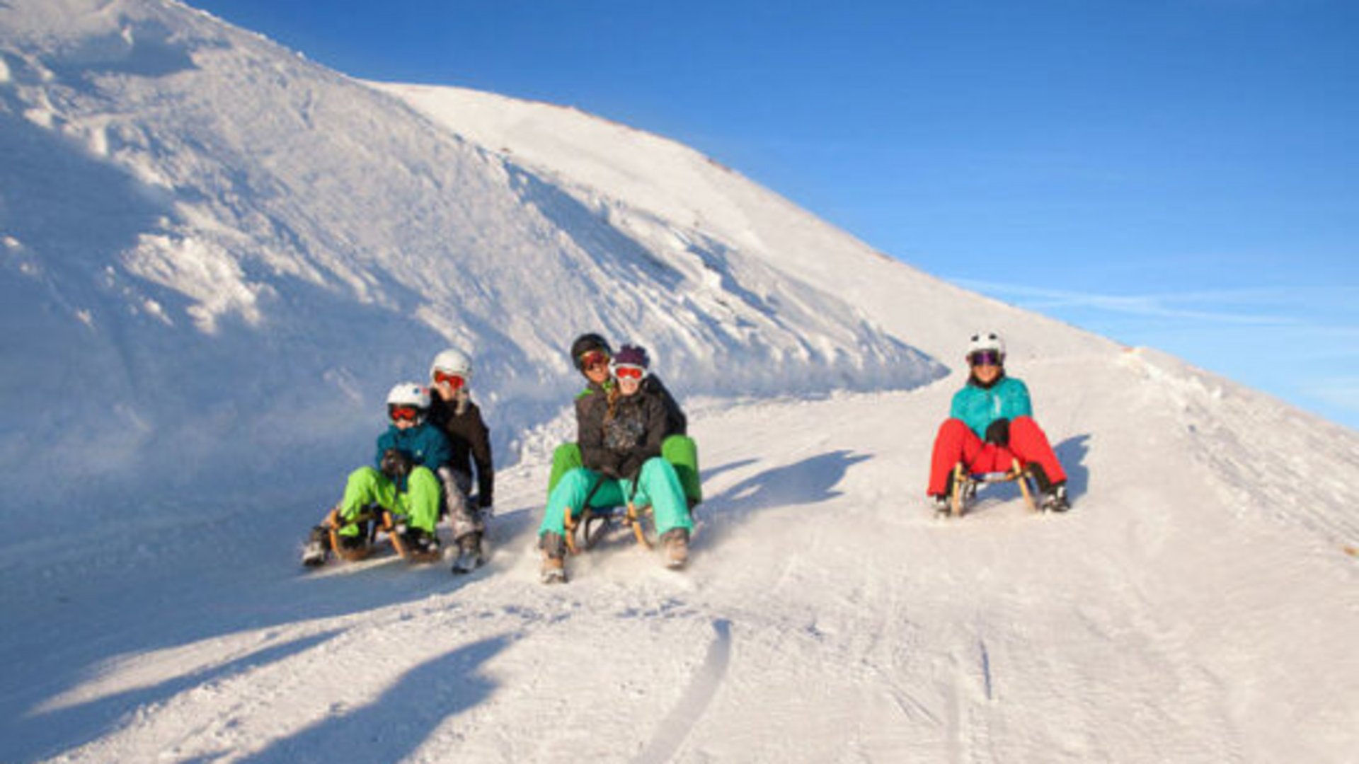 Salzburgerland: Winter im Smaragdhotel Tauernblick Familie rodelnd auf schneebedecktem Hang bei klarem Himmel