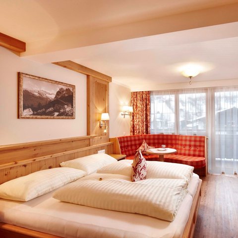 Erlebnis und Natur-Romantik im Hotel im Salzburgerland Gemütliches Hotelzimmer mit Doppelbett, roter Sitzecke und Bergbild an der Wand